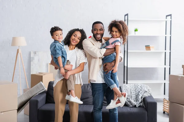 Happy african american couple holding kids in hands in new apartment — Stock Photo