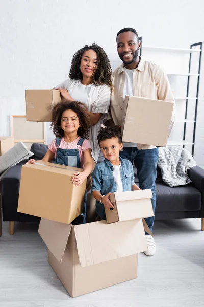 Happy african american family with carton boxes looking at camera in new apartment — Stock Photo