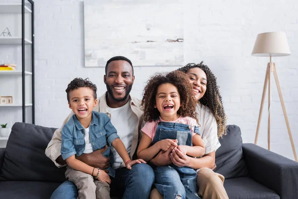 Familia afroamericana emocionada riendo en el sofá en casa - foto de stock