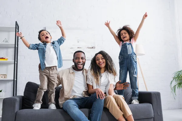 Crianças americanas africanas felizes mostrando gesto de sucesso perto dos pais no sofá em casa — Fotografia de Stock