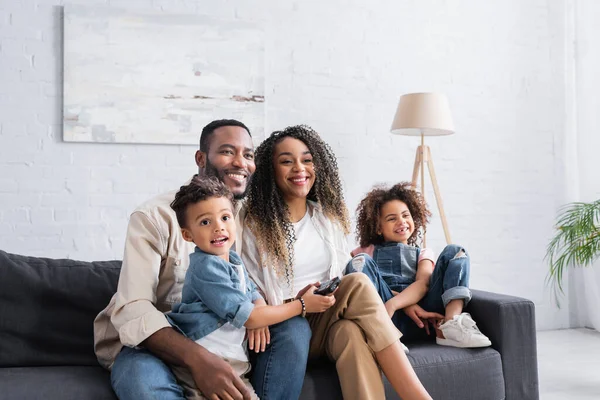 Familia afroamericana feliz viendo comedia en el sofá en casa - foto de stock
