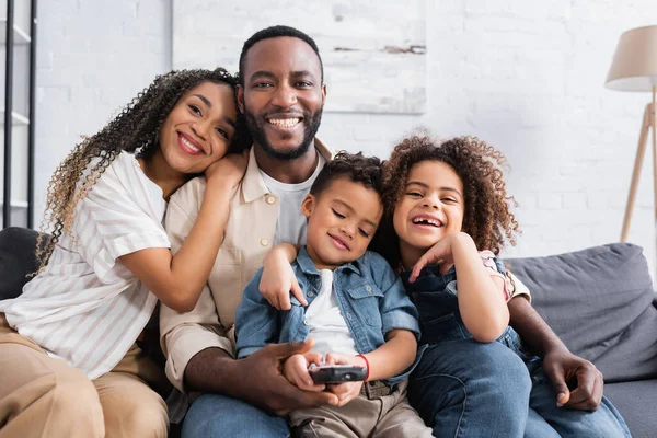 Mujer afroamericana feliz viendo la televisión con la familia en casa - foto de stock