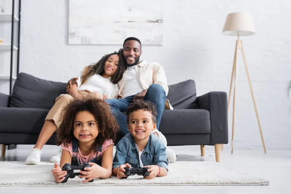 KYIV, UKRAINE - JANUARY 25, 2021: blurred african american couple looking at kids gaming on floor — Stock Photo