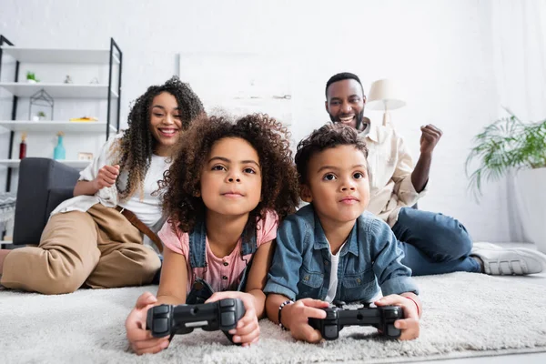 KYIV, UKRAINE - JANUARY 25, 2021: african american children gaming on floor near blurred parents — Stock Photo