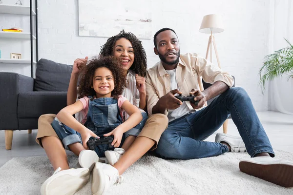 KYIV, UKRAINE - JANUARY 25, 2021: excited african american woman showing win gesture near gaming husband and daughter — Stock Photo