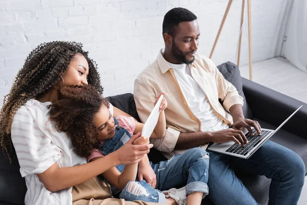 Menina americana africana usando laptop perto de mãe e pai digitando no laptop — Fotografia de Stock