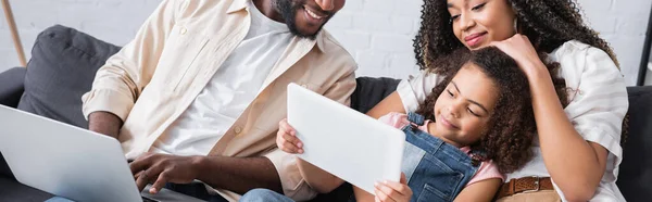 Africano americano pareja sonriendo cerca hija con digital tablet, bandera - foto de stock