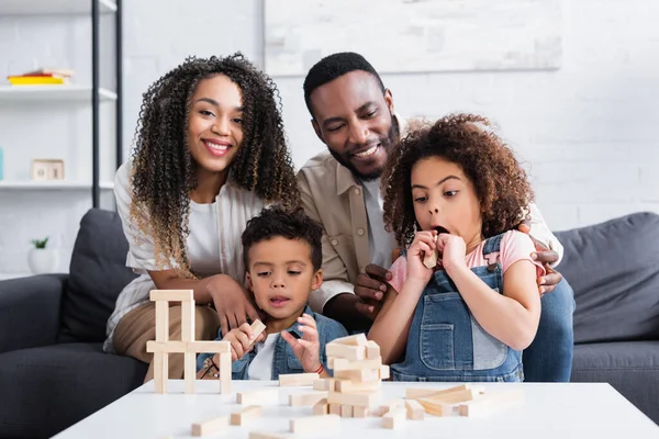 Étonné afro-américaine fille près souriant parents et frère jouer jeu de blocs en bois — Photo de stock
