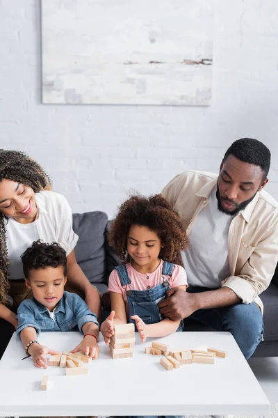 Pareja afroamericana mirando a los niños jugando bloques de madera juego - foto de stock