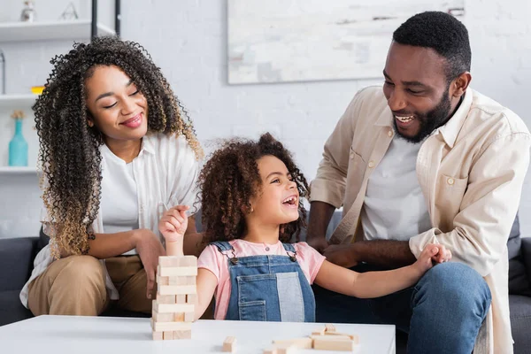 Веселая африканская американская девушка улыбается рядом счастливые родители и деревянные блоки игры — стоковое фото