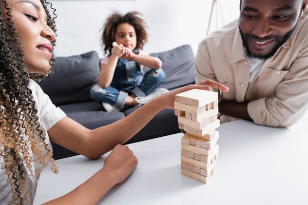 African american couple playing wooden blocks game near daughter sitting on sofa on blurred background — Stock Photo