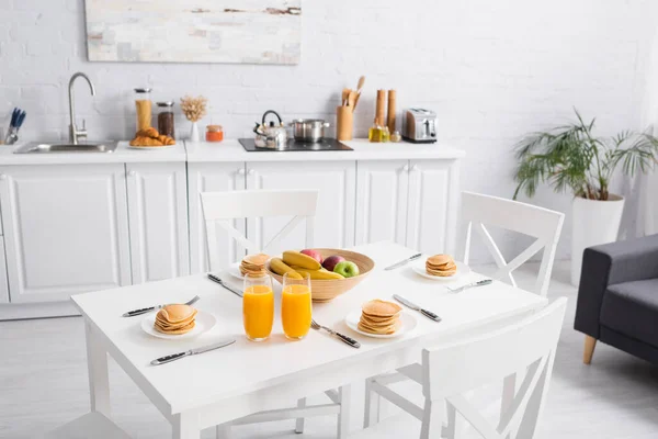 Fresh orange juice, tasty pancakes and fruits on table in modern kitchen — Stock Photo