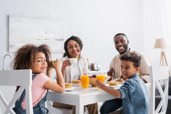 Familia afroamericana feliz sonriendo a la cámara durante el desayuno - foto de stock