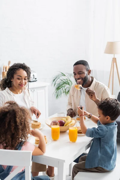 Glückliches afrikanisch-amerikanisches Paar isst Pfannkuchen beim Frühstück mit Kindern — Stockfoto