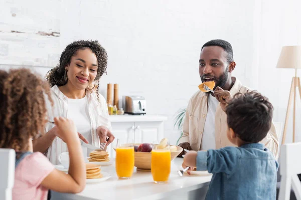 Casal afro-americano tomando café da manhã com crianças desfocadas na cozinha — Fotografia de Stock