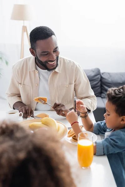 Happy african american man eating pancakes near son and blurred daughter — Stock Photo