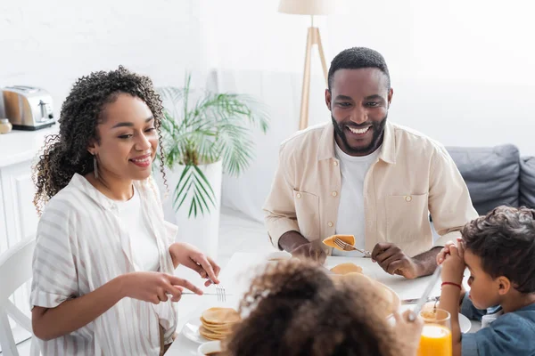 Couple afro-américain souriant pendant le petit déjeuner avec des enfants flous — Stock Photo