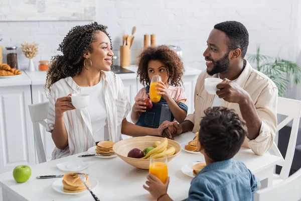 Menina afro-americana beber suco de laranja durante o café da manhã com a família — Fotografia de Stock