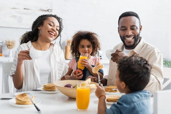 Africano americano ragazza holding mela e arancia succo vicino felice genitori e blurred fratello — Foto stock