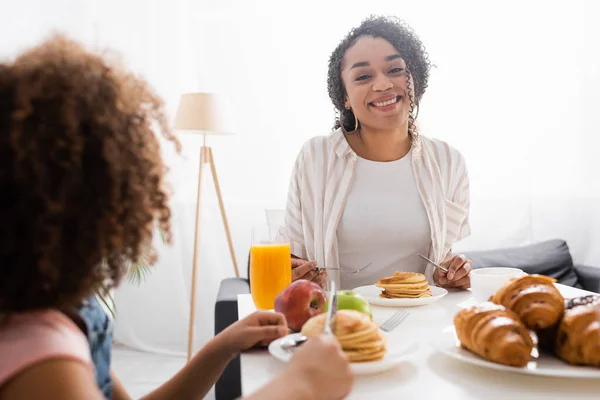 Glückliche afrikanisch-amerikanische Frau lächelt beim Frühstück neben verschwommener Tochter — Stockfoto