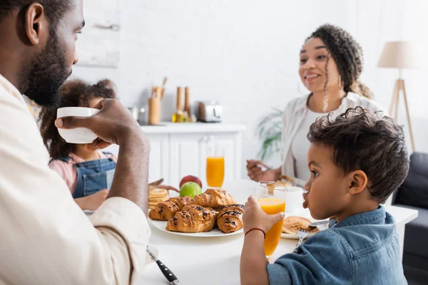 Afrikanischer amerikanischer Junge trinkt Orangensaft beim Frühstück mit der Familie — Stockfoto