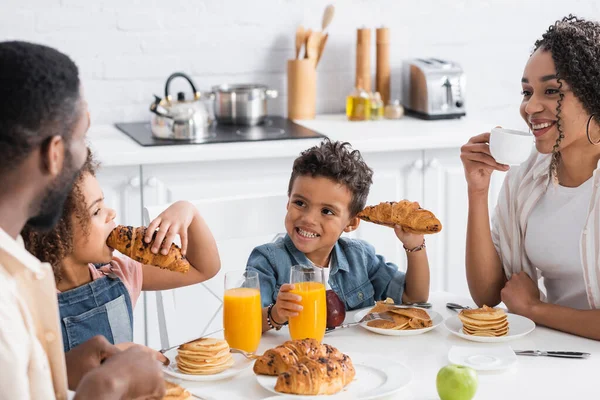 Афріканський американець посміхається, коли тримає круассан під час сніданку з родиною. — стокове фото