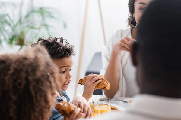 Emocionado afroamericano chico celebración croissant cerca borrosa familia - foto de stock