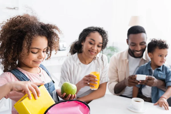 Africano americano chica embalaje mochila cerca padres y hermano en cocina - foto de stock