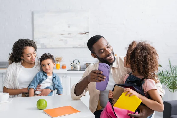 Afrikanisch-amerikanischer Mann packt Rucksack mit Tochter nahe Familie in Küche — Stockfoto