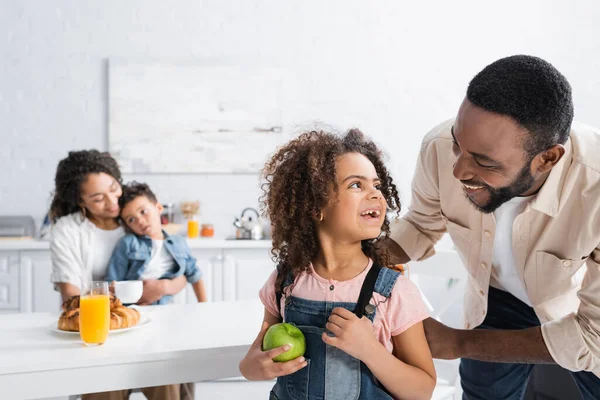 Afrikanisch-amerikanischer Mann lächelt neben Tochter mit Apfel und Rucksack — Stockfoto