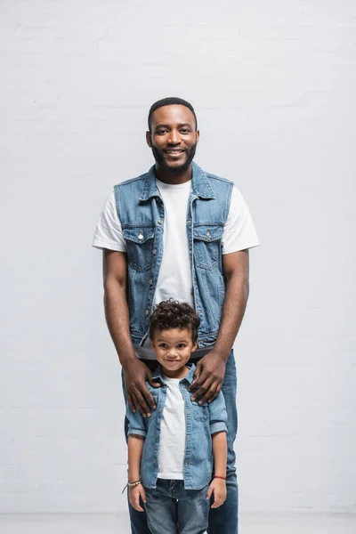 Feliz afroamericano padre e hijo mirando la cámara en gris - foto de stock