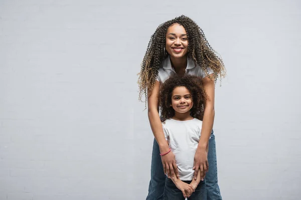 Vue de face de femme afro-américaine avec enfant regardant la caméra sur gris — Photo de stock