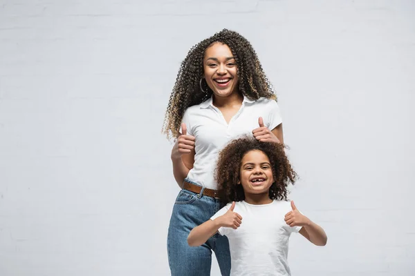 Emocionado afroamericano chica con mamá mostrando pulgares hacia arriba en gris - foto de stock