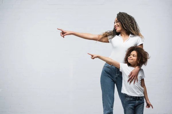 Souriant afro-américaine mère et fille regardant de côté et pointant du doigt sur gris — Photo de stock