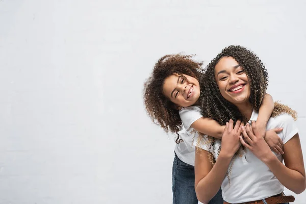 Fröhliches Kind umarmt glückliche afrikanisch-amerikanische Mutter auf grau — Stockfoto