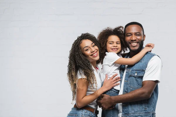 Familia afroamericana feliz sonriendo a la cámara mientras se abraza en gris - foto de stock