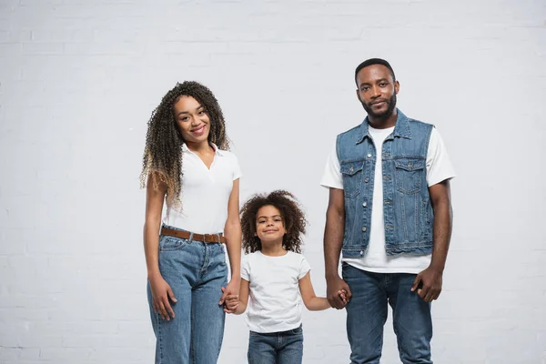 Glückliches afrikanisch-amerikanisches Paar hält die Hände seiner Tochter auf grau — Stockfoto