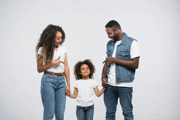 Cheerful african american parents pointing at daughter on grey — Stock Photo