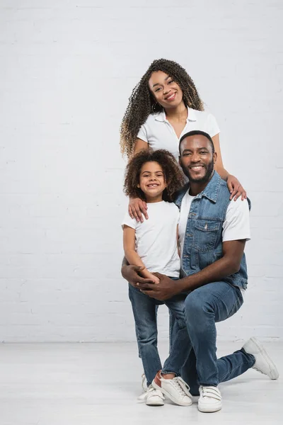 Visão de comprimento total da família afro-americana abraçando enquanto sorri para a câmera em cinza — Fotografia de Stock