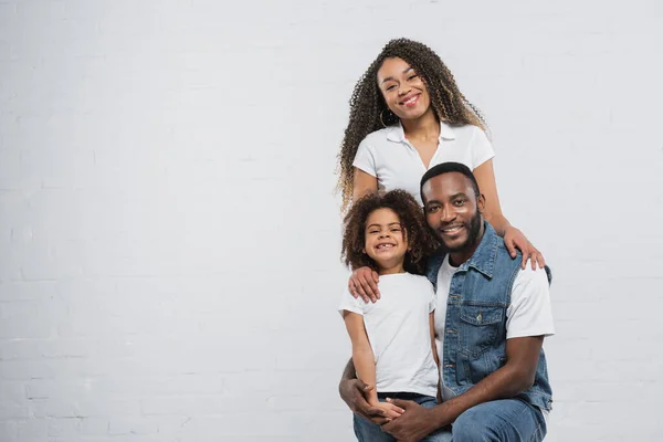 African american man hugging daughter near happy wife on grey — Stock Photo