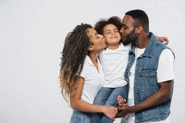 Afrikanisch-amerikanisches Paar küsst Tochter mit geschlossenen Augen auf grau — Stockfoto