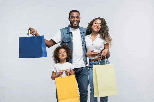 Família americana africana satisfeito com sacos de compras multicoloridos sorrindo para a câmera no cinza — Fotografia de Stock