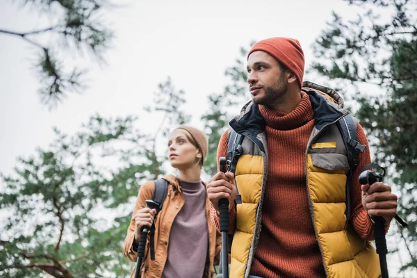 Man holding hiking sticks and standing near blurred girlfriend with backpack — Stock Photo