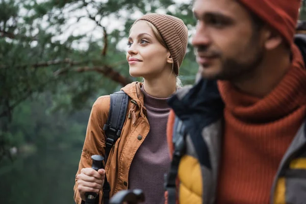 Glückliche Frau hält Wanderstock neben Freund im verschwommenen Vordergrund — Stockfoto