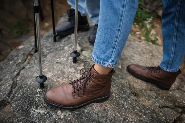 Vista cortada de mulher e homem de botas com bengalas de caminhada em pé na rocha — Fotografia de Stock