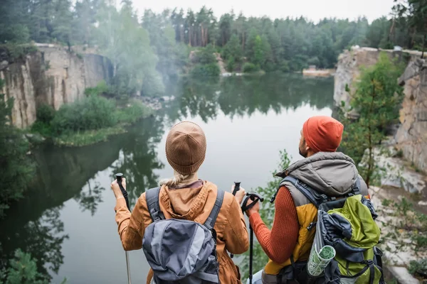 Visão traseira do casal com mochilas perto do lago na floresta — Fotografia de Stock