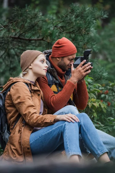 Mulher sentada com namorado tirando foto na câmera vintage na floresta — Fotografia de Stock