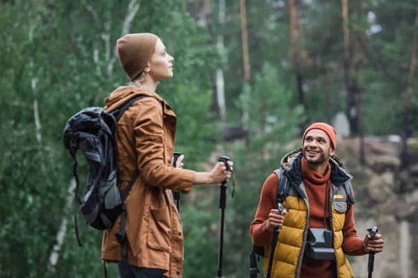 Happy man with vintage camera looking at woman holding hiking sticks in forest — Stock Photo