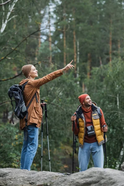 Mujer feliz señalando con el dedo cerca de novio trekking en el bosque - foto de stock