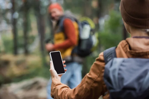 Frau hält Smartphone während leerer Bildschirm in der Nähe verschwommener Mann im Wald — Stockfoto